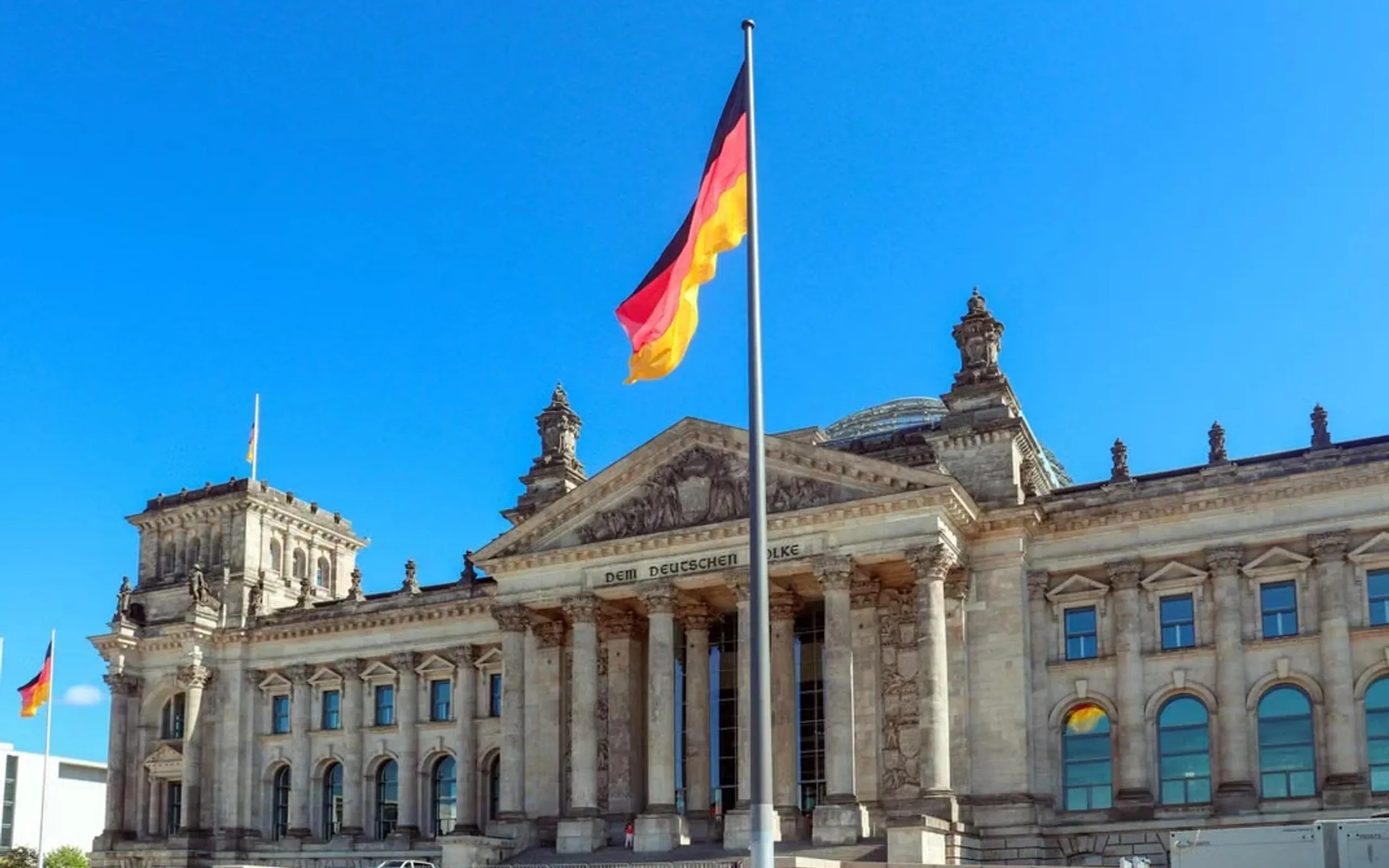 Reichstagsgebäude in Berlin mit Deutschlandflagge vor blauem Himmel, Sitz des Deutschen Bundestages