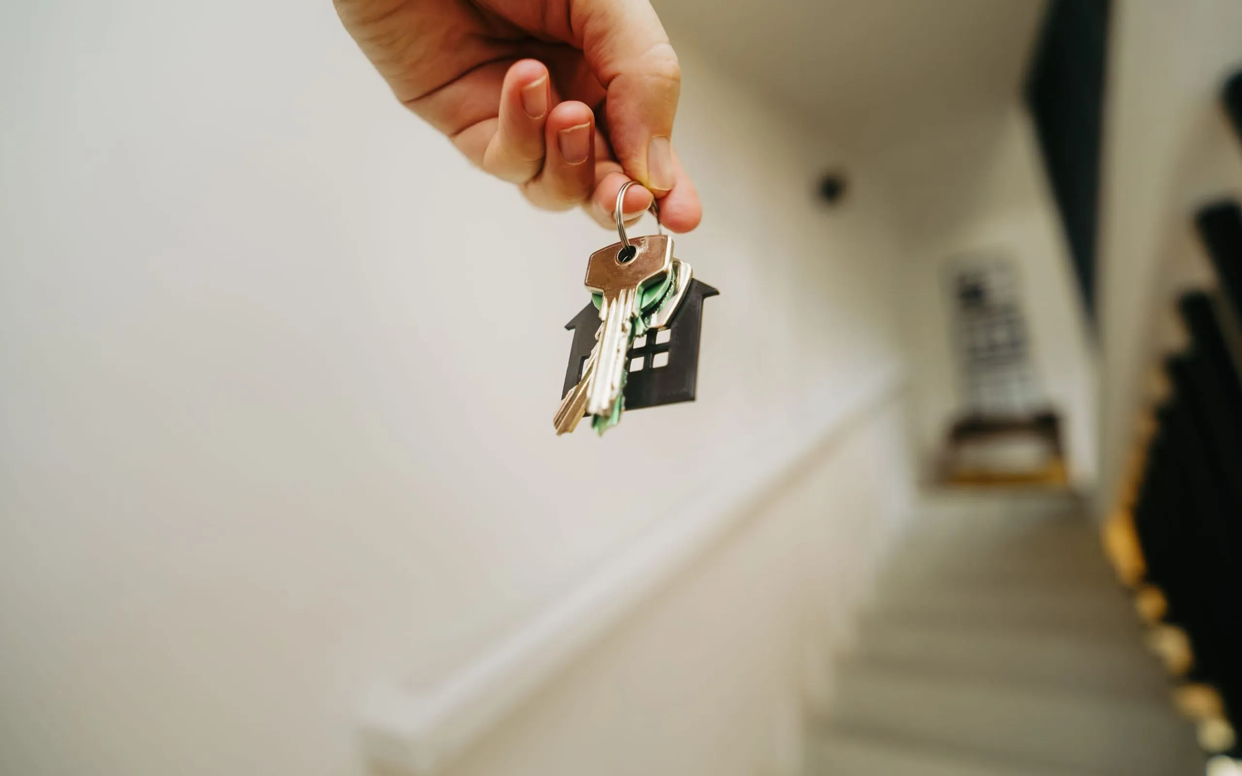 Vermieter hält den Wohnungsschlüssel mit Haus-Anhänger im Treppenhaus einer Mietwohnung